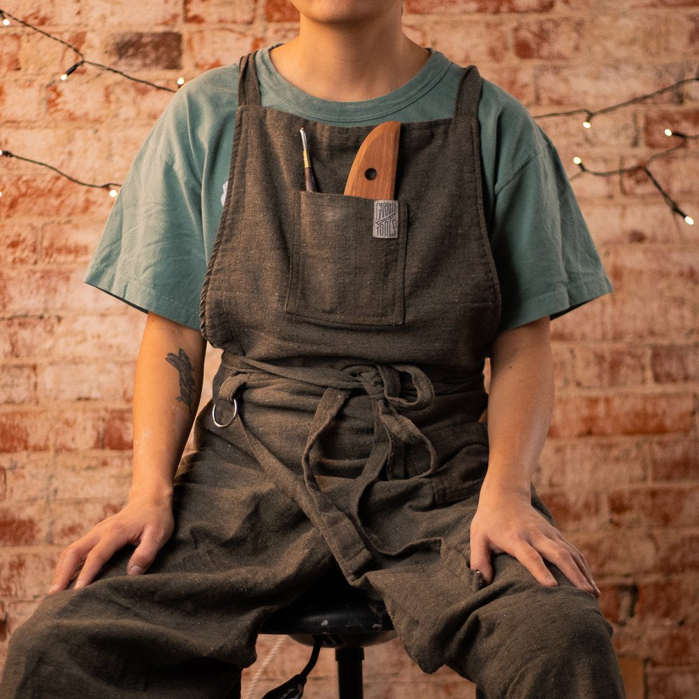 person sitting on stool wearing a cotton potter's apron