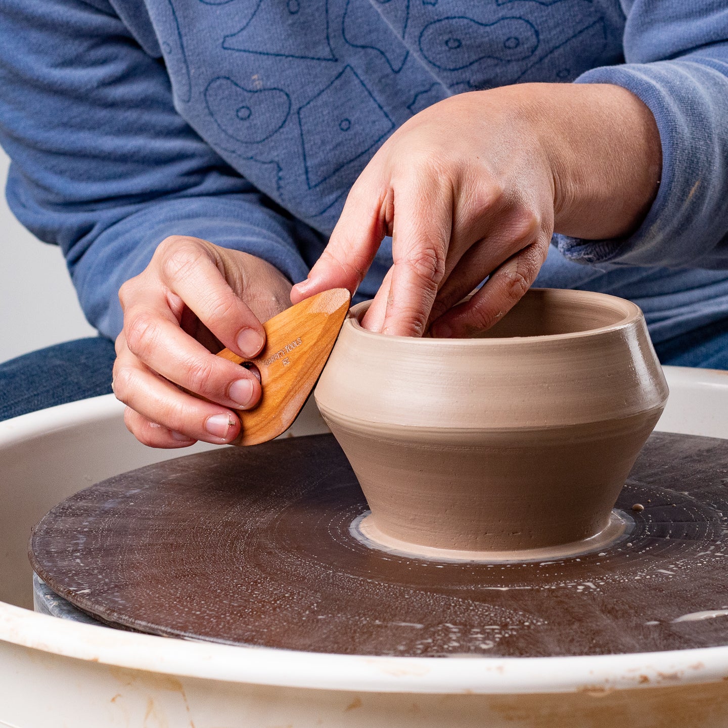 ceramicist using Garrity Tools B2 wooden pottery rib on potter's wheel