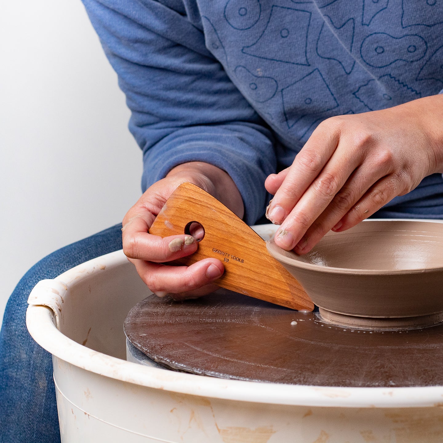 Ceramicist using Garrity Tools B3 wooden pottery rib on clay pot