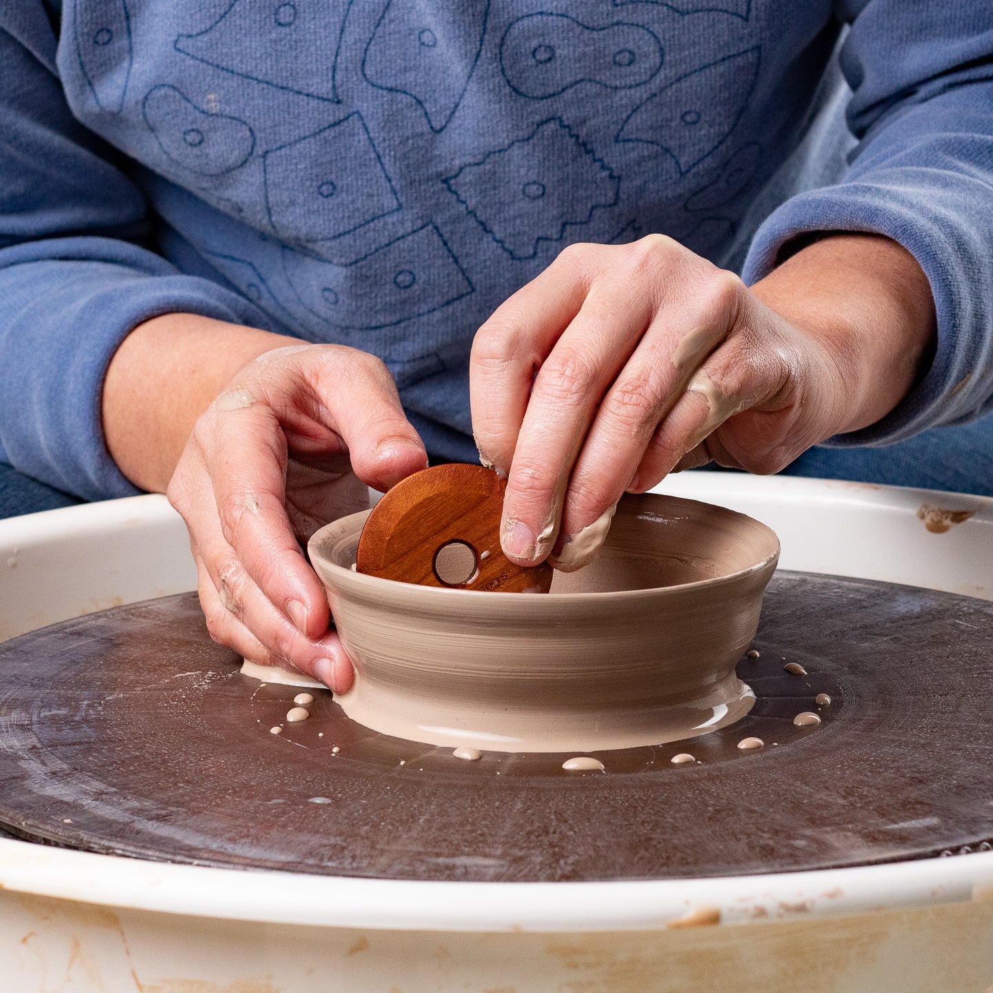 ceramicist using Garrity Tools C1 wooden pottery rib on clay pot