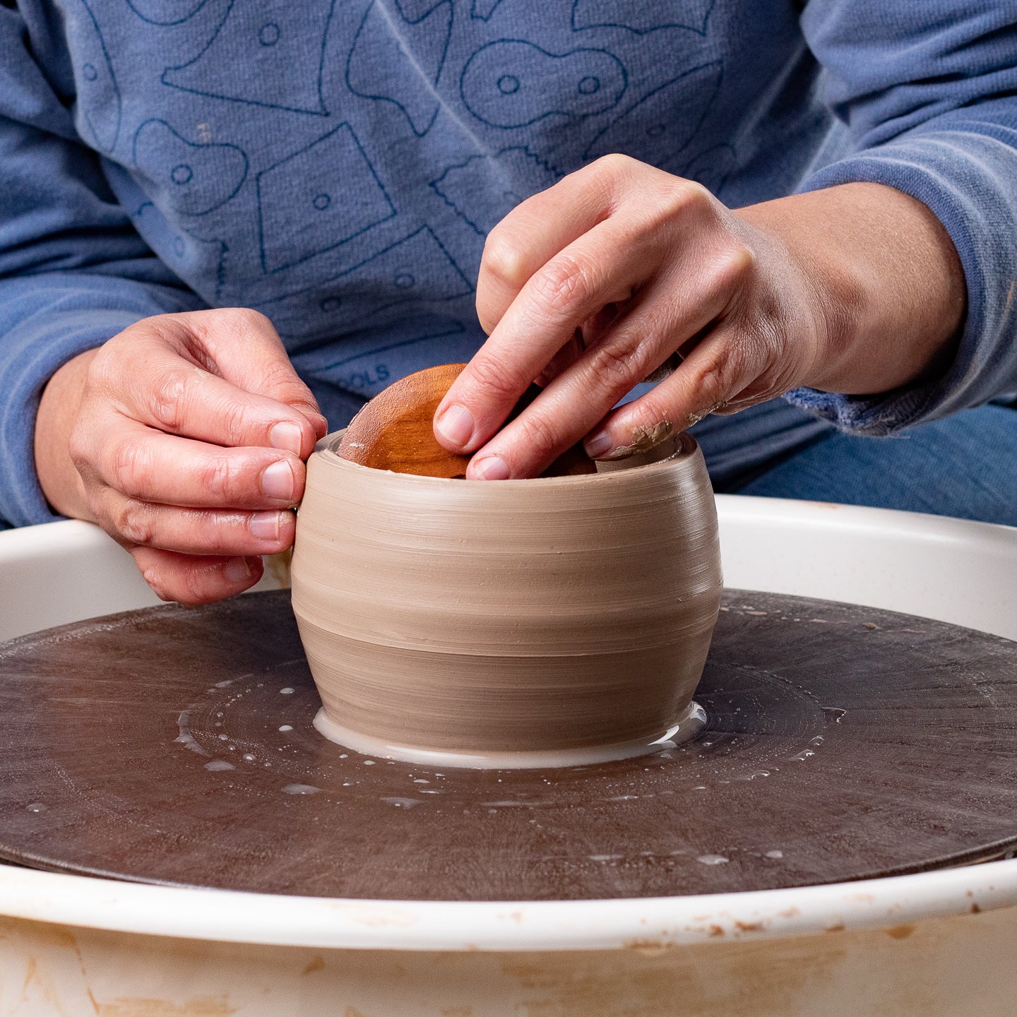 ceramicist using Garrity Tools C3 wooden pottery rib on clay pot