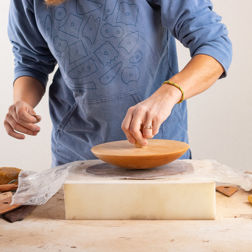 potter pushing wood anvil top into a clay slab on a piece of foam