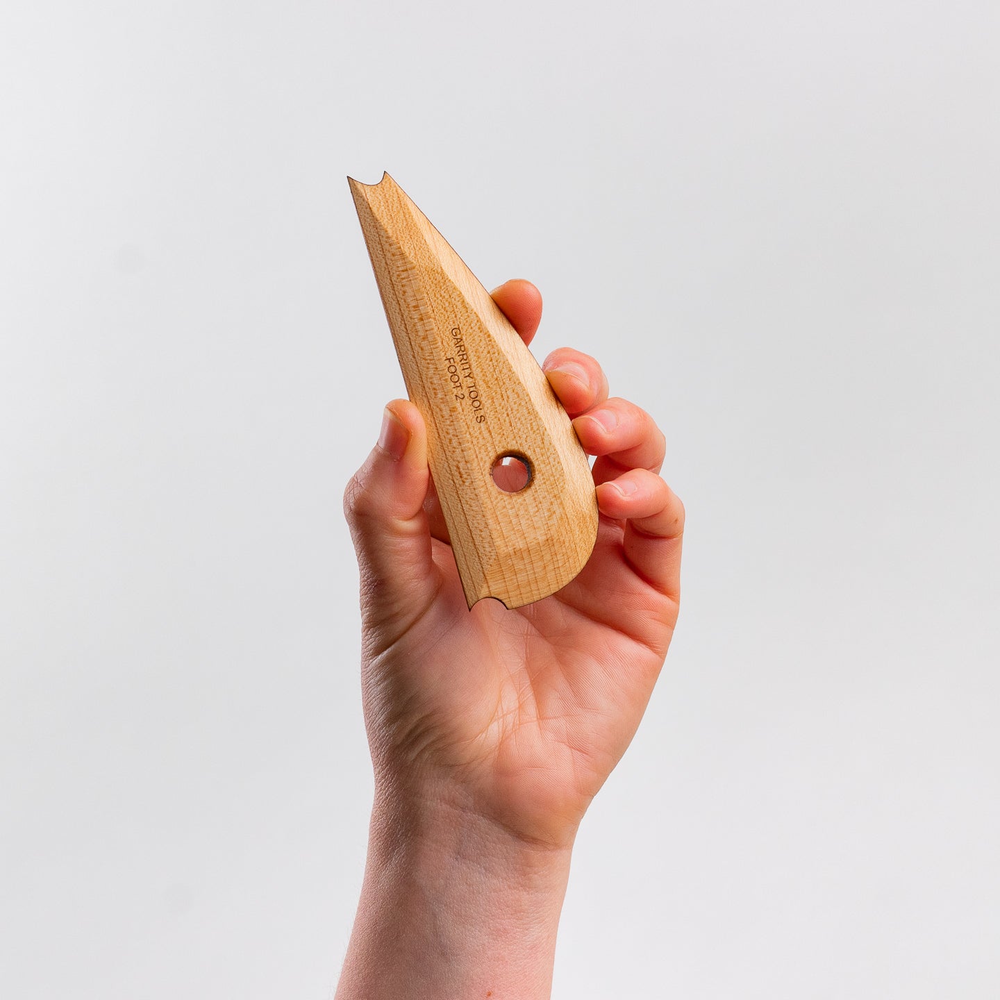 hand holds Garrity Tools Foot 2 wooden pottery tool on white background