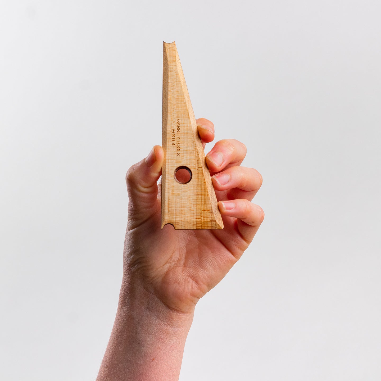 hand holds Garrity Tools Foot 4 wooden pottery tool on white background