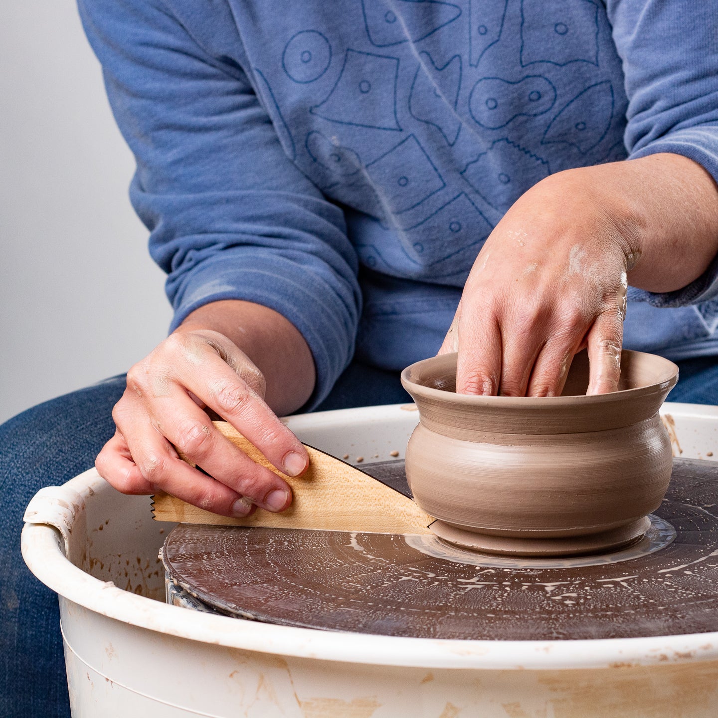 ceramicist uses Garrity Tools Foot 5 wooden pottery tool on clay pot