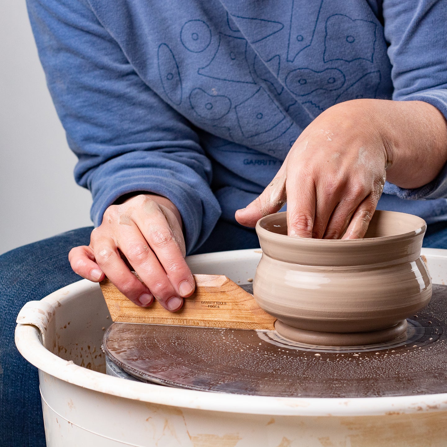 ceramicist uses Garrity Tools Foot 6 wooden pottery tool on clay pot