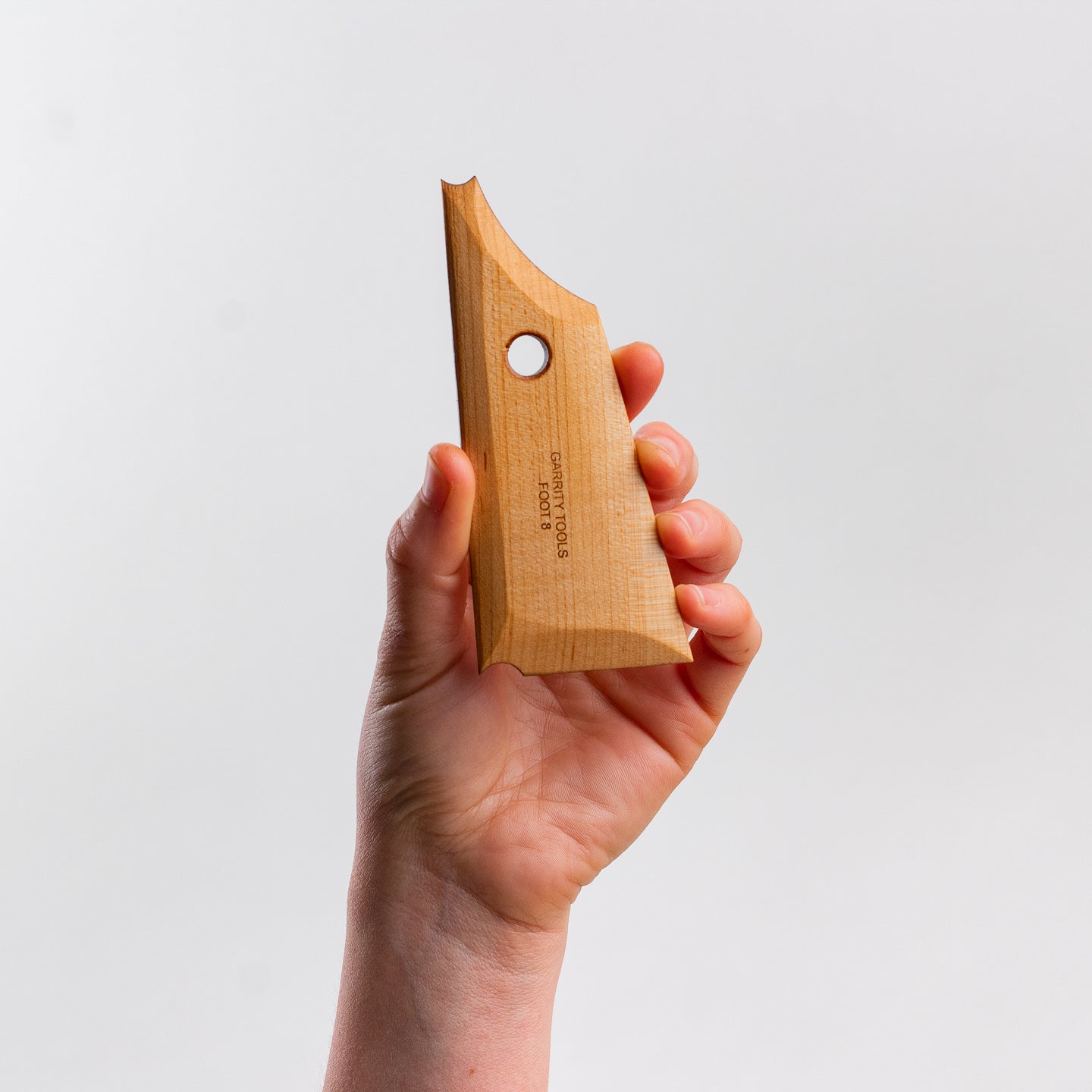 hand holds Garrity Tools Foot 8 wooden pottery tool on white background