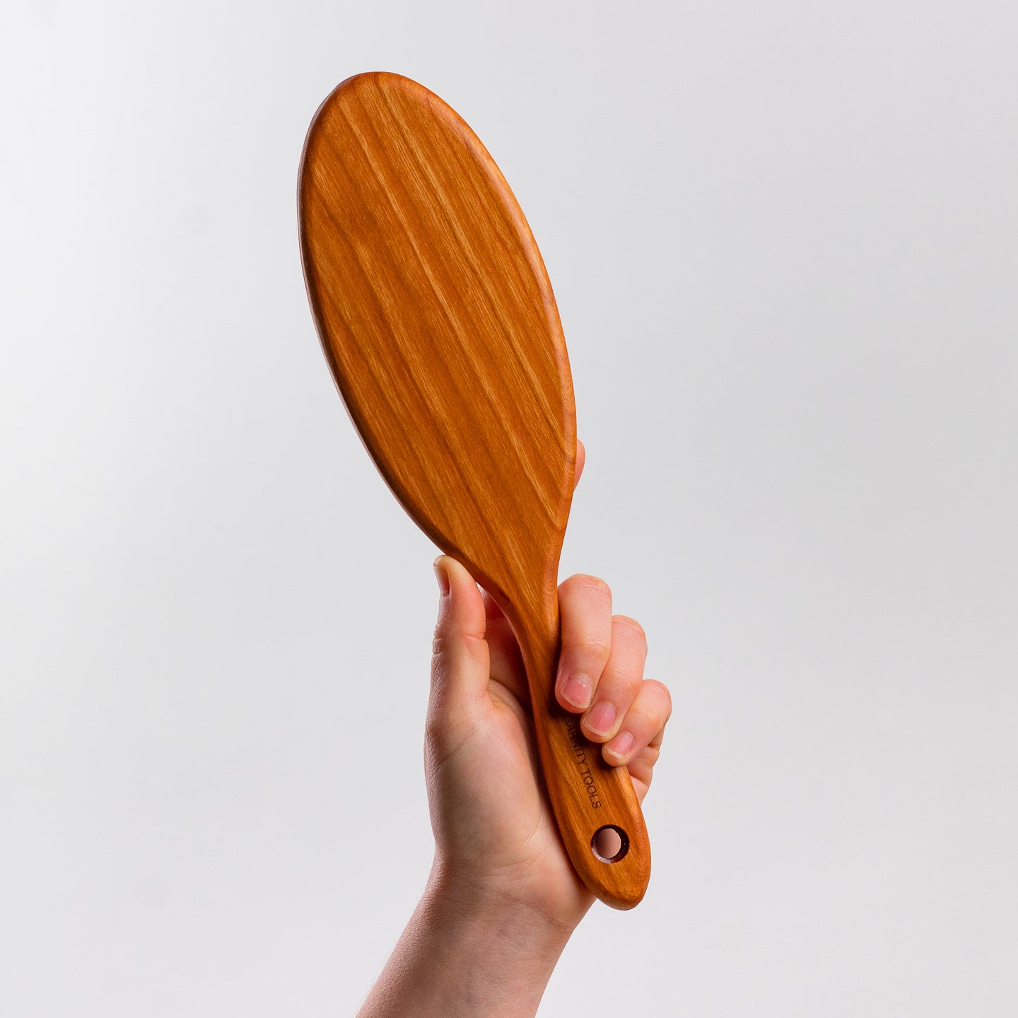 hand holds Garrity Tools wooden paddle pottery tool on white background