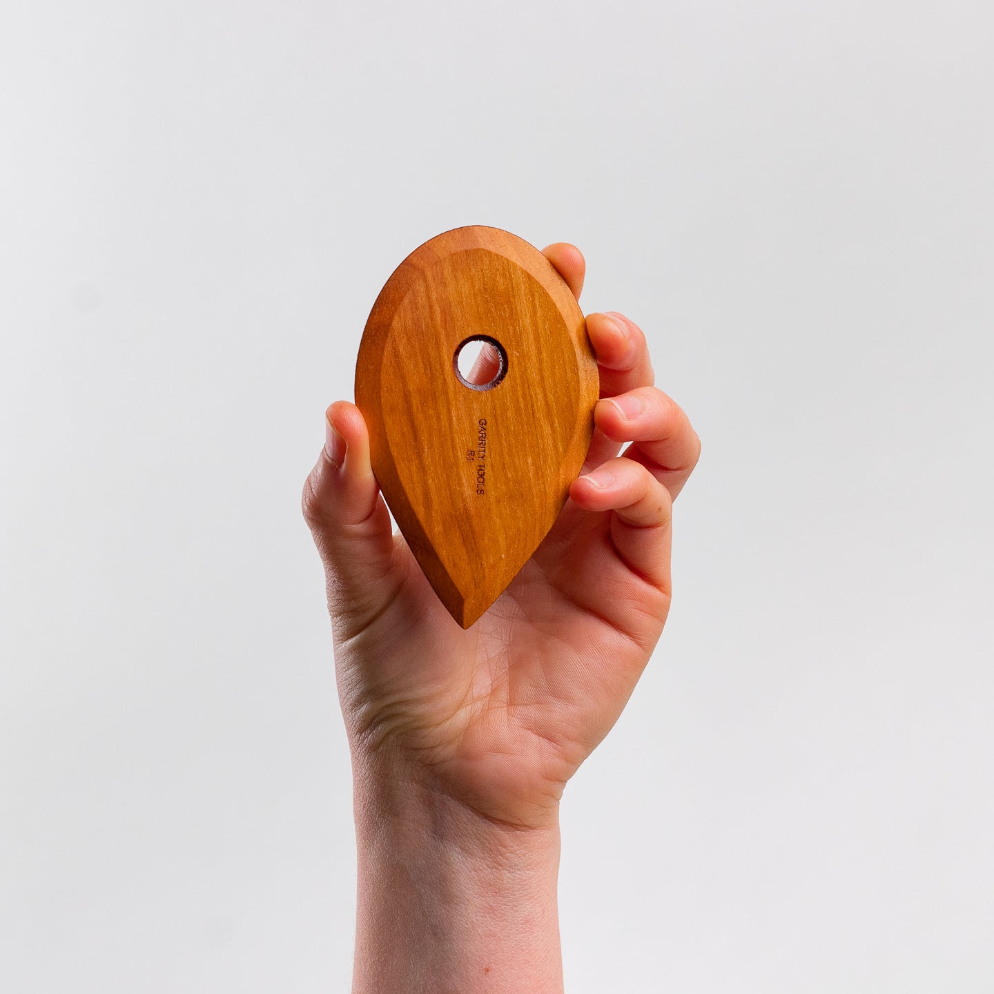 hand holds Garrity Tools R1 wooden pottery tool on white background