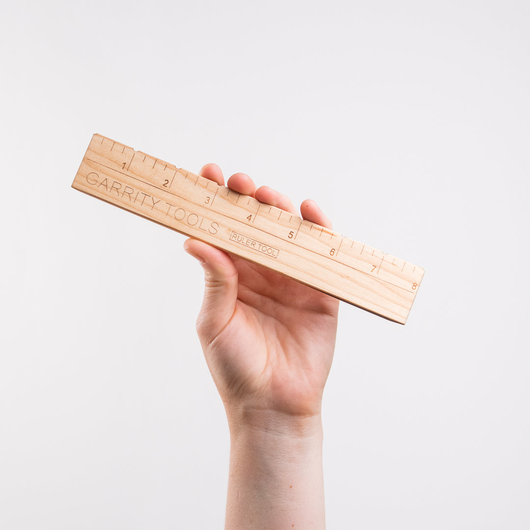 hand holds Garrity Tools Ruler wooden pottery tool on white background