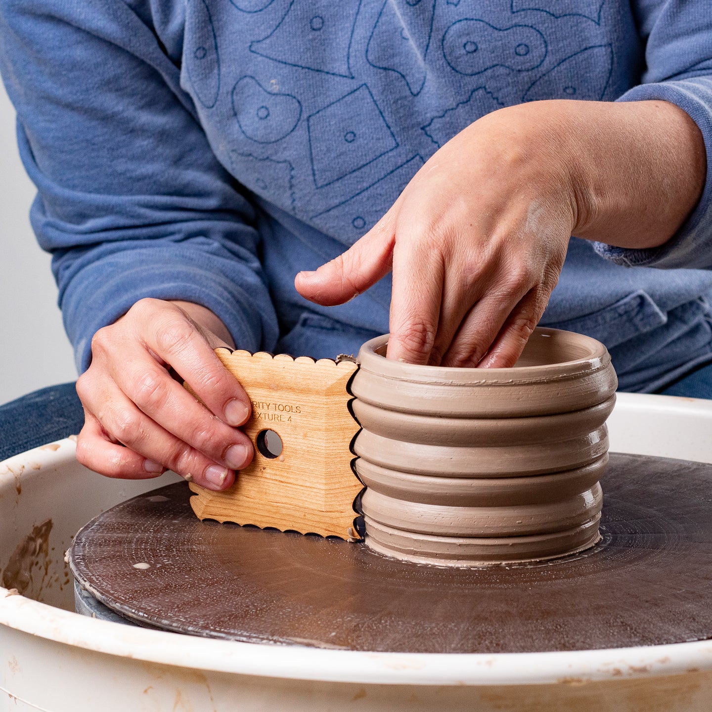 ceramicist uses Garrity Tools Texture 4 wooden pottery tool on clay cylinder