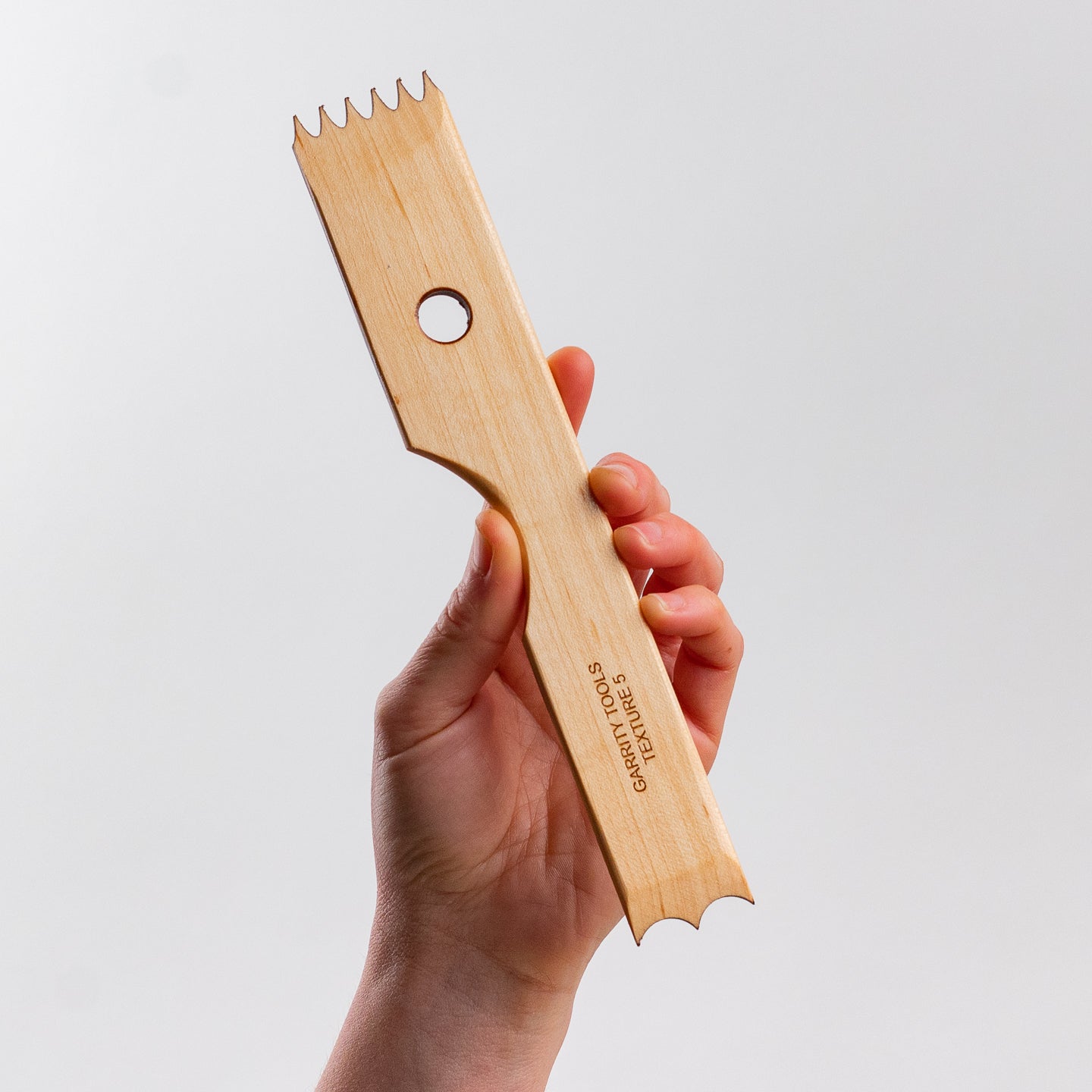 hand holds Garrity Tools Texture 5 wooden pottery tool on white background