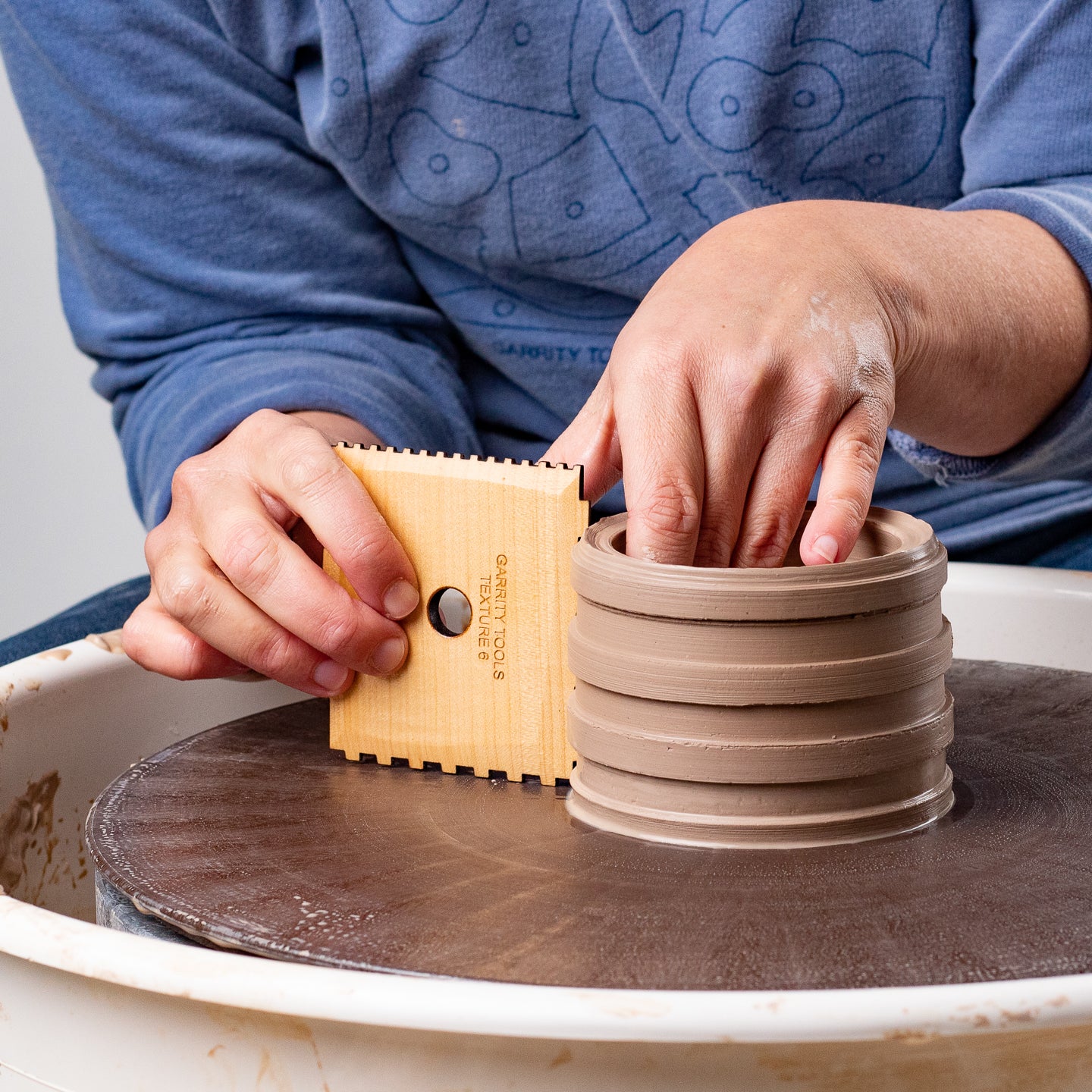 ceramicist uses Garrity Tools Texture 6 wooden pottery tool on clay cylinder 