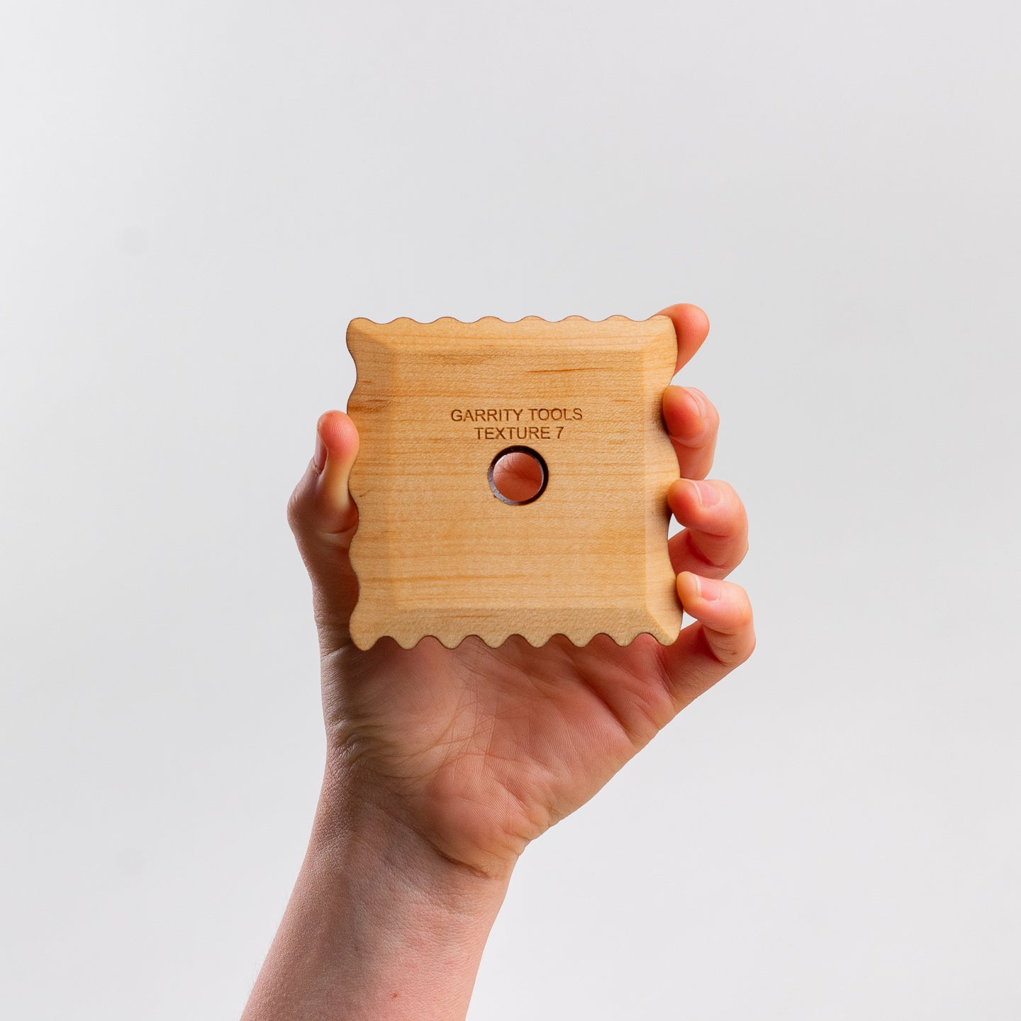 hand holds Garrity Tools Texture 7 wooden pottery tool on white background