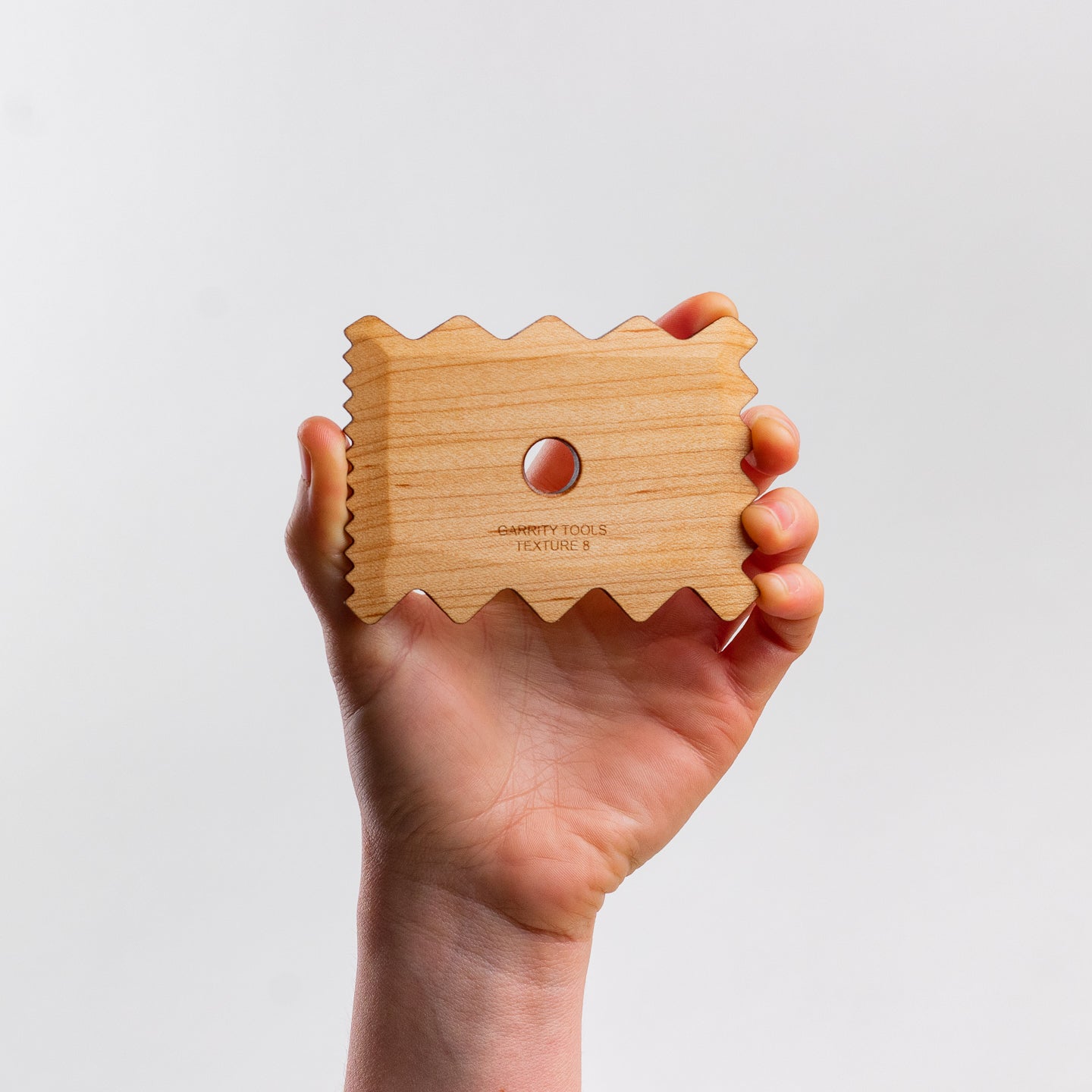 hand holds Garrity Tools Texture 7 wooden pottery tool on white background