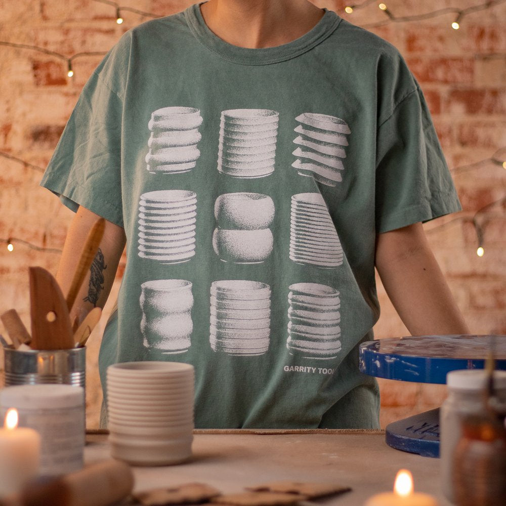 person wearing green t-shirt with screen printed white pottery pieces on the front