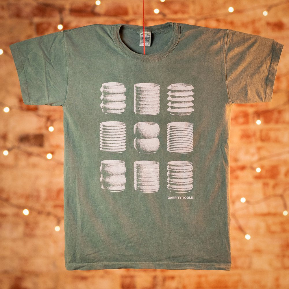 green t-shirt screenprinted with white pottery pieces in front of brick wall