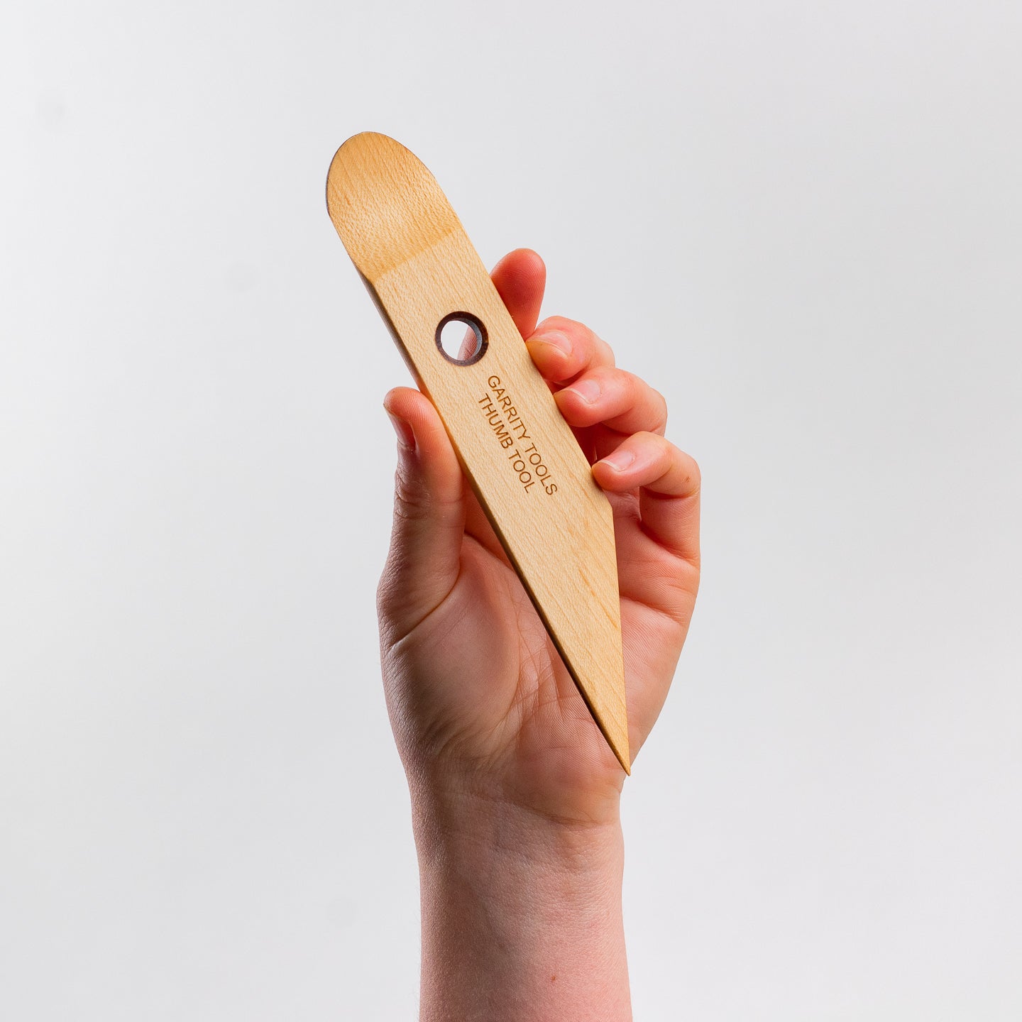 hand holds Garrity Tools Thumb wooden pottery tool on white background