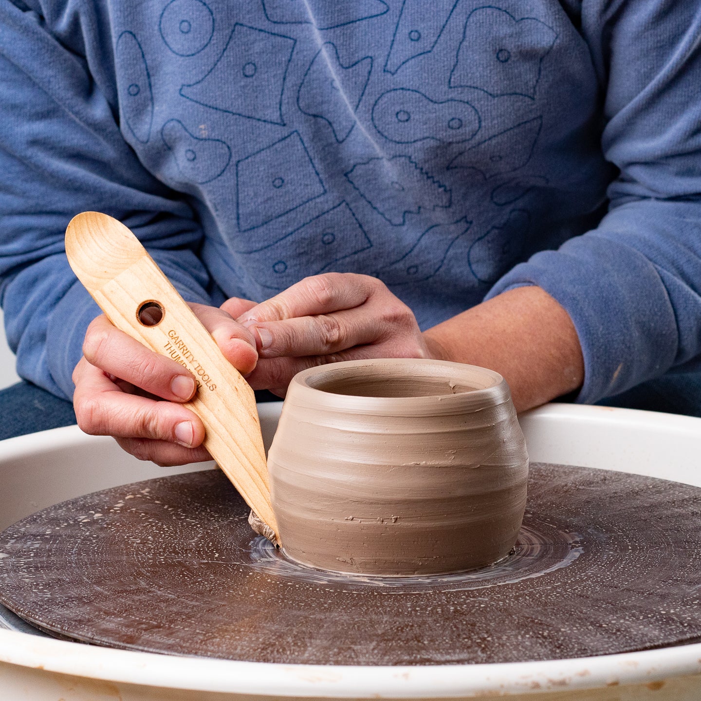 ceramicist uses Garrity Tools Thumb wooden pottery tool to trim clay bowl