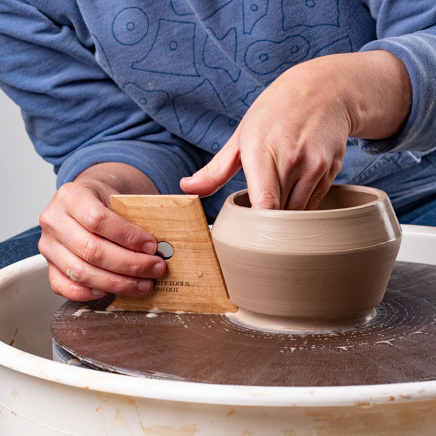 ceramicist uses Garrity Tools Unfoot 1 wooden pottery tool on clay pot