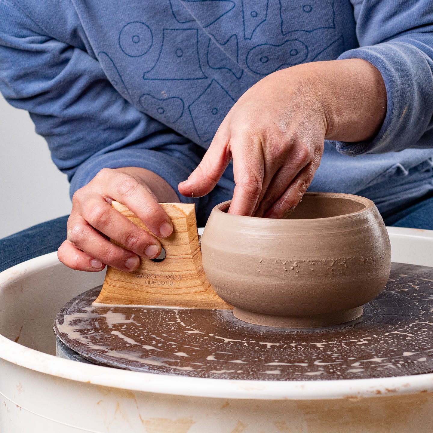 ceramicist uses Garrity Tools Unfoot 2 wooden pottery tool on clay pot